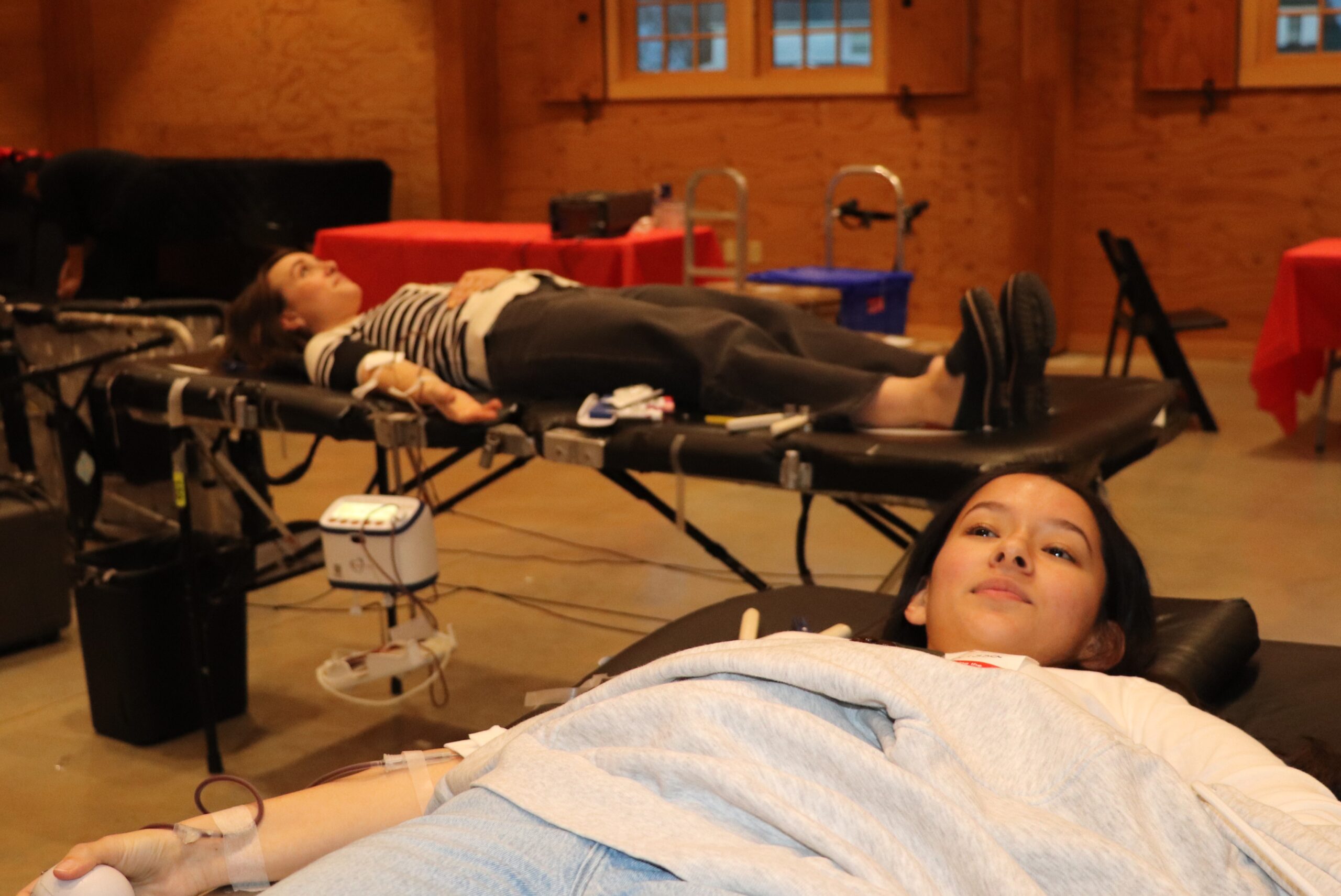 Two women lie on tables donating blood at a blood drive.