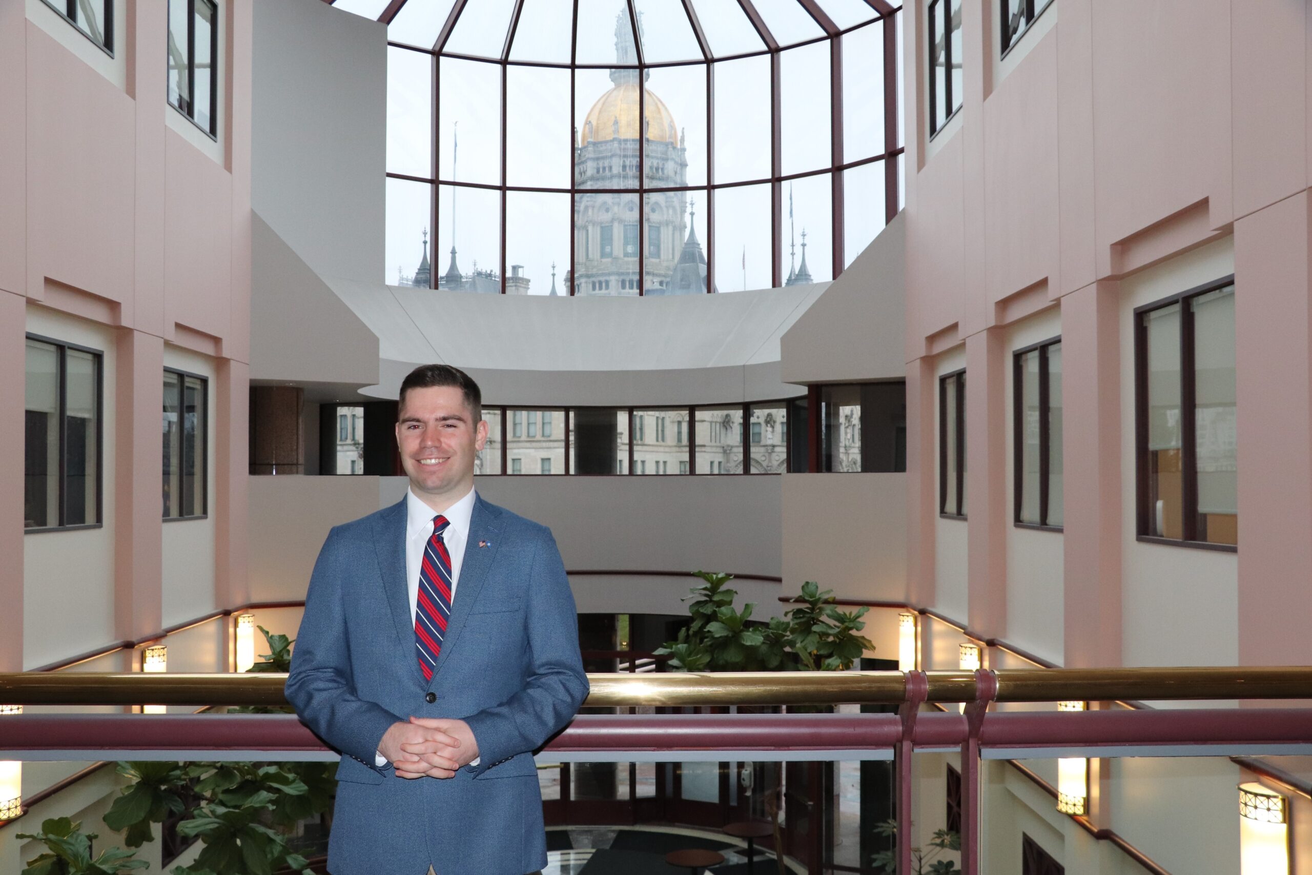 Matthew Keatley, legislative intern, stands in the Legislative Office Building with the Connecticut Capitol Building in the background.